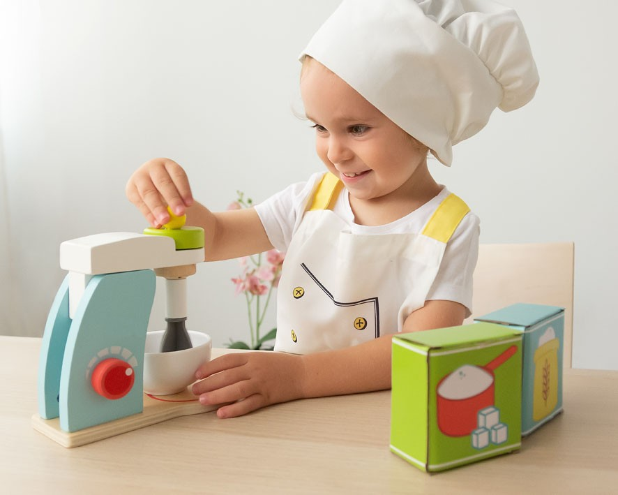 Criança a brincar com brinquedo de cozinha em madeira e avental branco com chapéu de chef