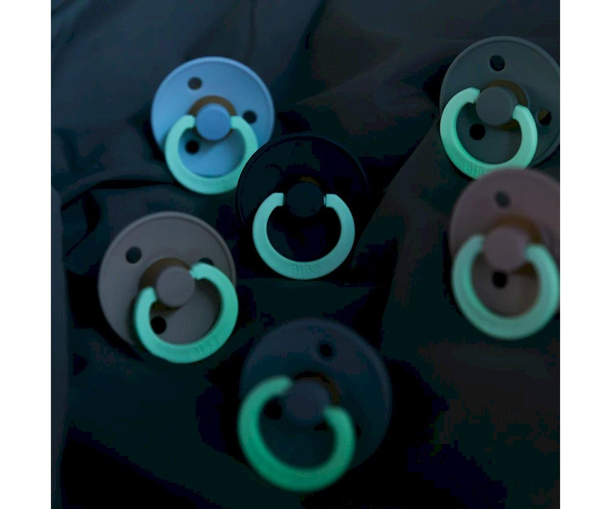 Seis chupetas de silicone em tons azul, verde e castanho sobre tecido escuro.