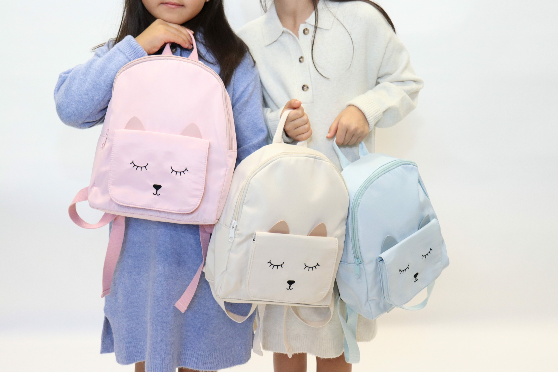 Mochilas infantis coloridas com rosto de gato e crianças a segurá-las