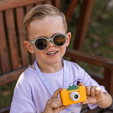 Criança com óculos de sol segurando uma câmara fotográfica laranja em forma de abacaxi