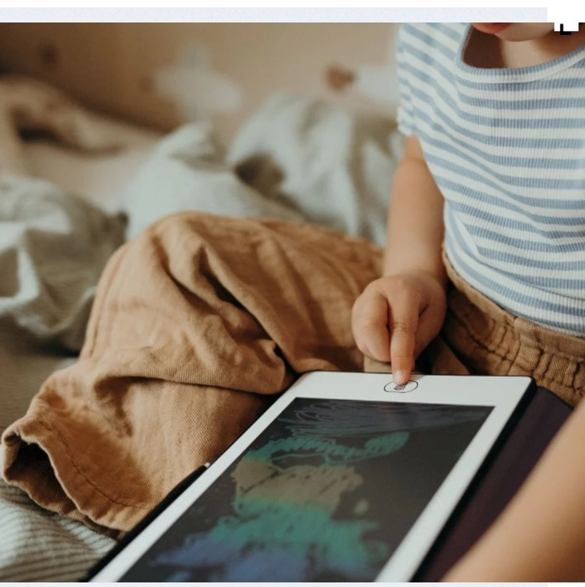 Criança a usar tablet numa cama com roupa de cama verde e branca.