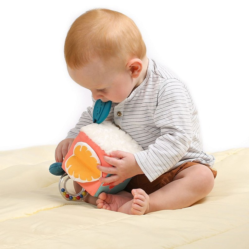 Bebé sentado a brincar com brinquedo macio colorido numa almofada amarela