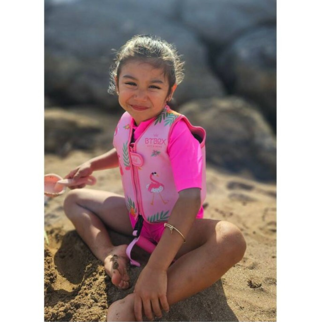 Criança com colete salva-vidas rosa sentada na areia da praia