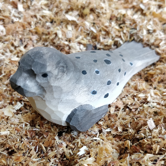 Figura decorativa de pássaro em madeira cinza com manchas pretas sobre aparas de madeira