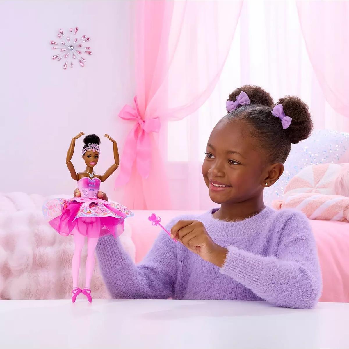 Boneca bailarina Barbie vestida de rosa ao lado de menina sorridente num quarto infantil rosa