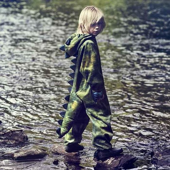 Criança com macacão verde camuflado e espinhos a caminhar em pedras junto a um rio