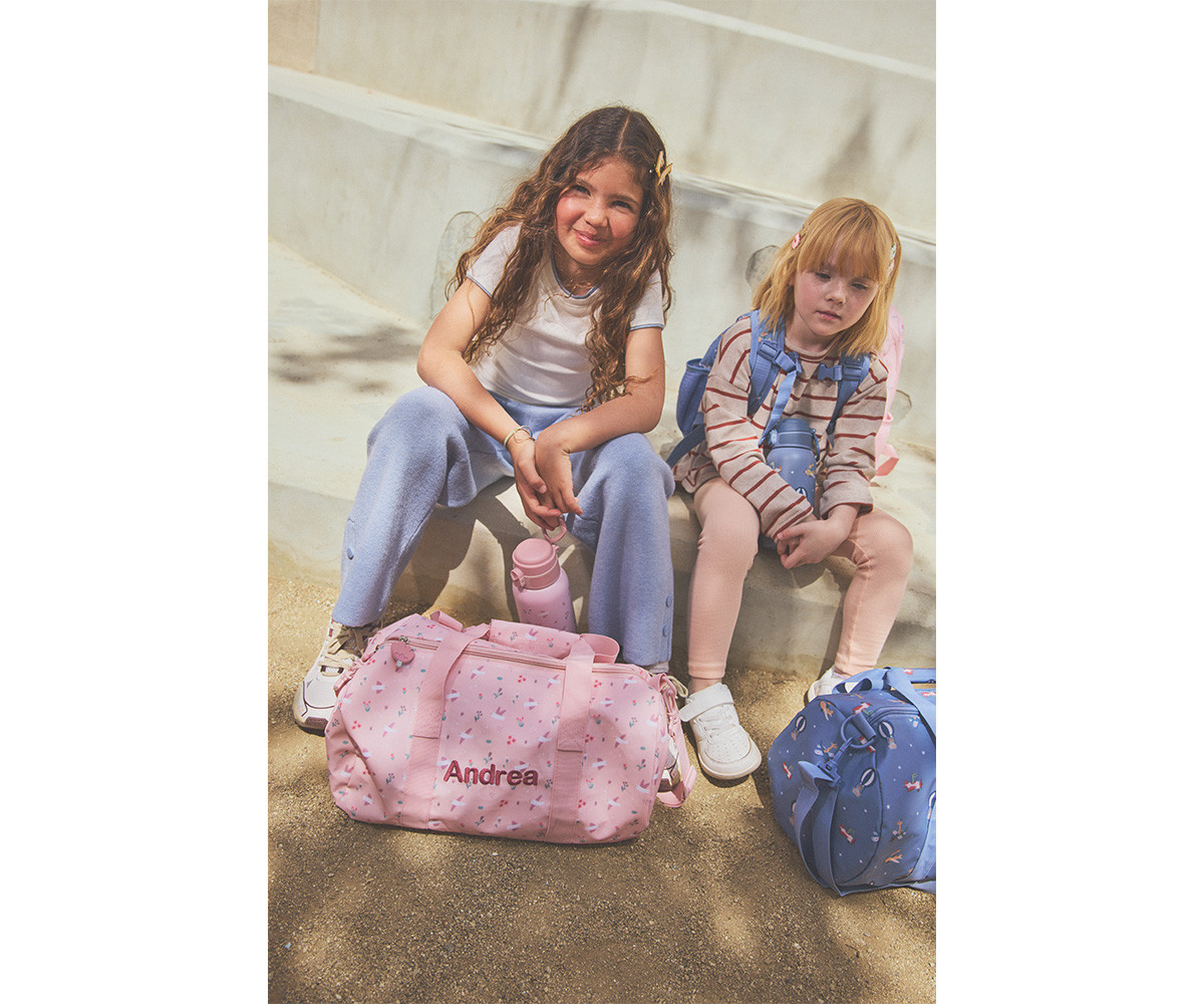 Duas crianças sentadas com mochilas rosa e azul em escadaria exterior