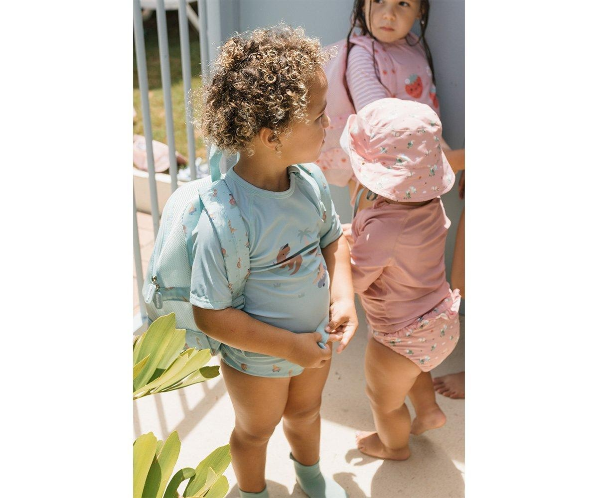 Crianças pequenas em fatos de banho coloridos em espaço exterior junto a vedação branca