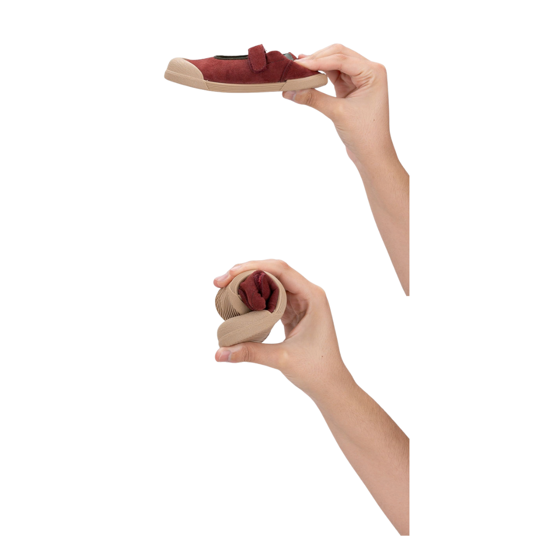 Sapato infantil vermelho com sola beige e fecho de velcro nas mãos, fundo branco.