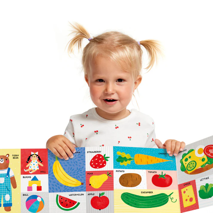 Criança com t-shirt branca a segurar tapete colorido com frutas e brinquedos