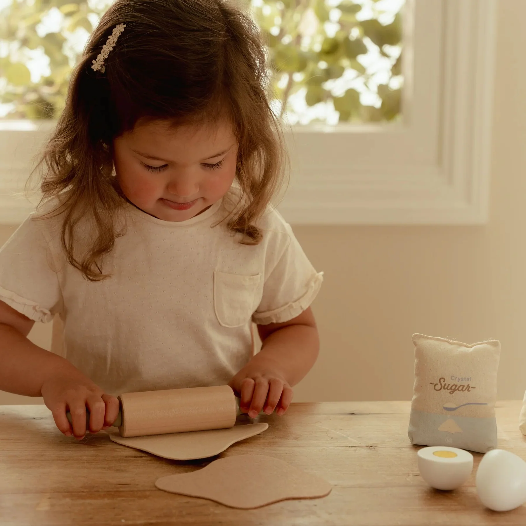 Criança a usar rolo de madeira para achatar massa com embalagem de Crystal Sugar e ovos de brinquedo