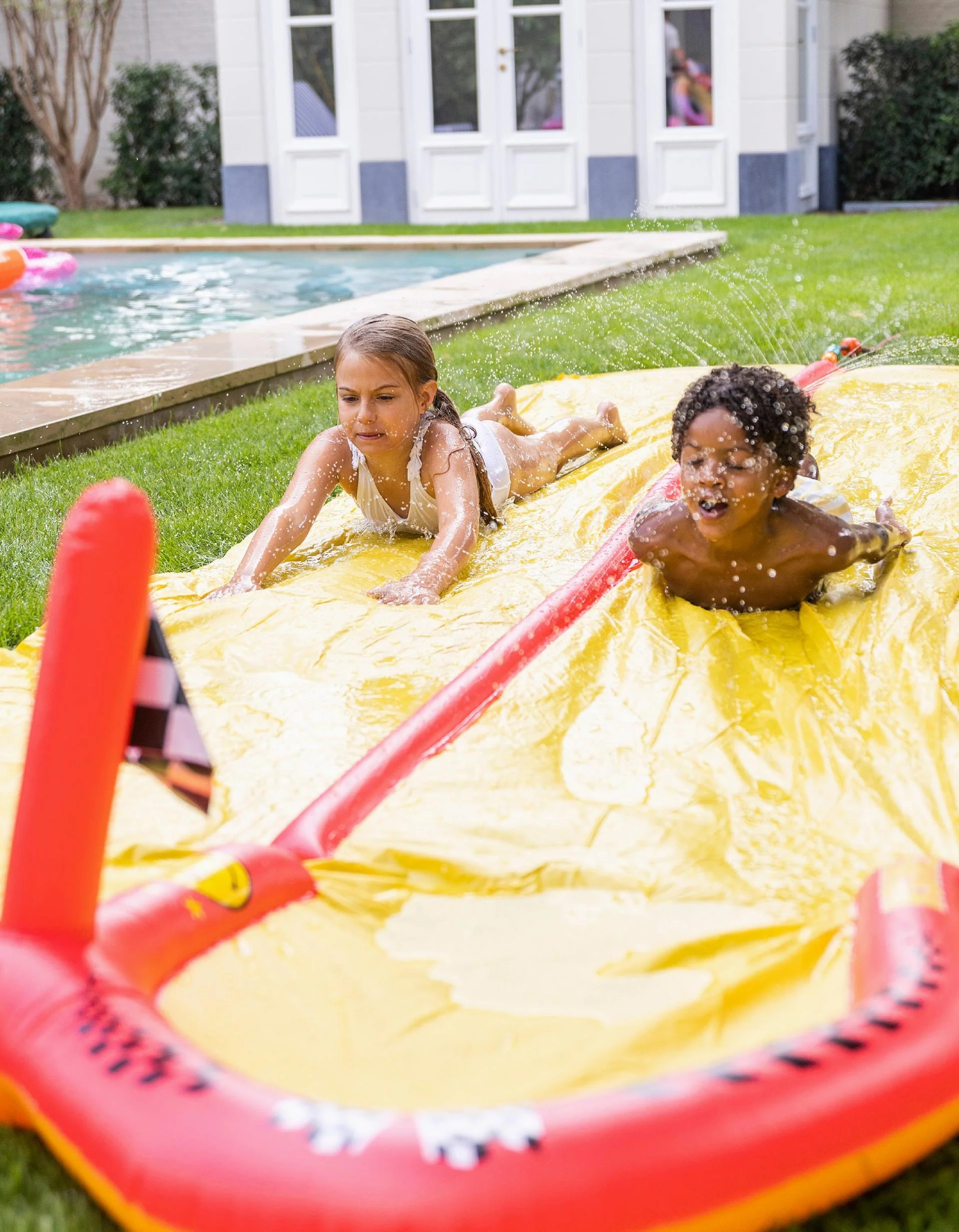 Crianças a escorregar num escorrega insuflável amarelo no jardim próximo de piscina