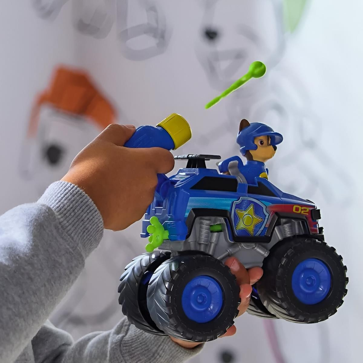 Brinquedo veículo azul com figura cão e projétil verde nas mãos de criança