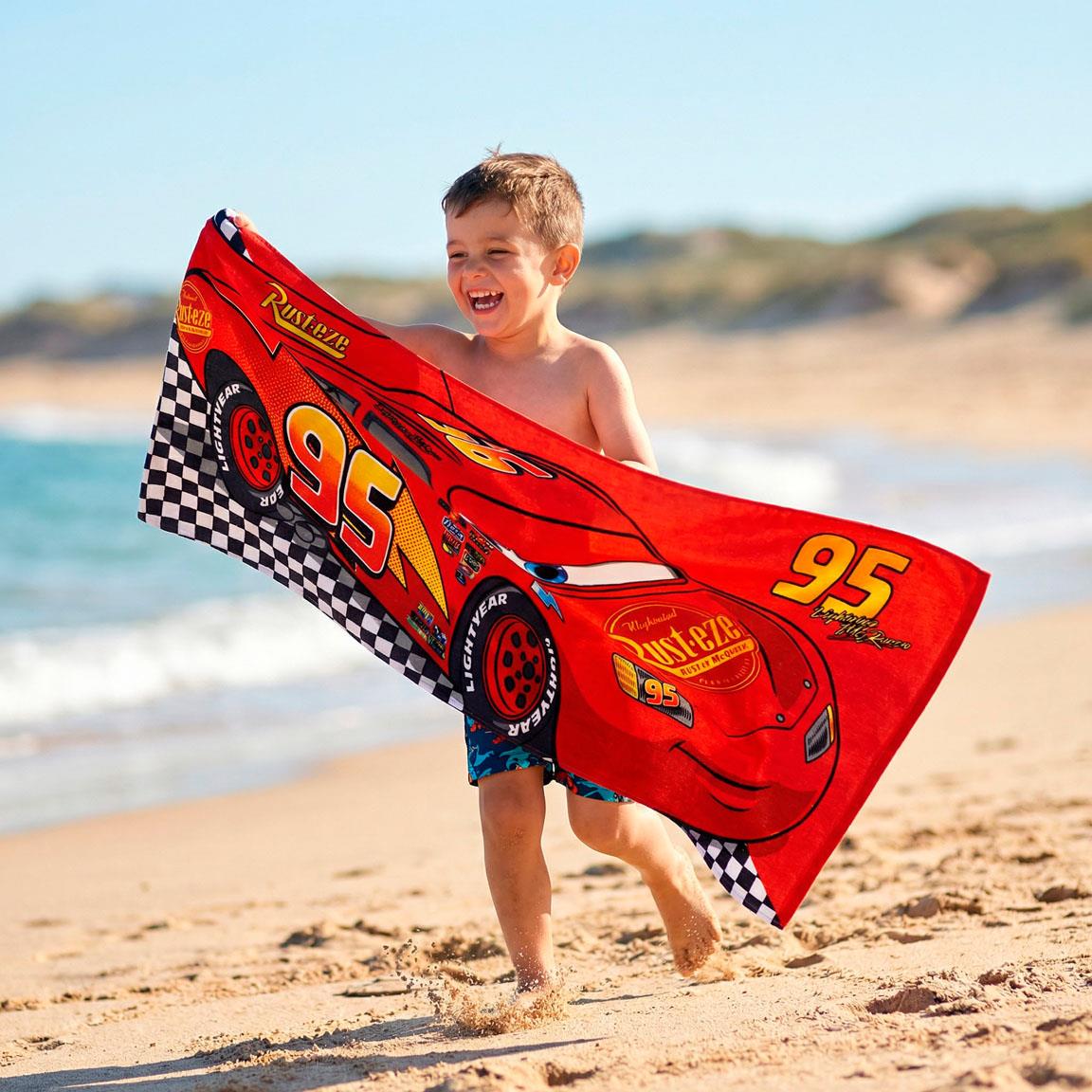Toalha infantil vermelha com estampa do carro Lightning McQueen e padrão quadriculado na praia.