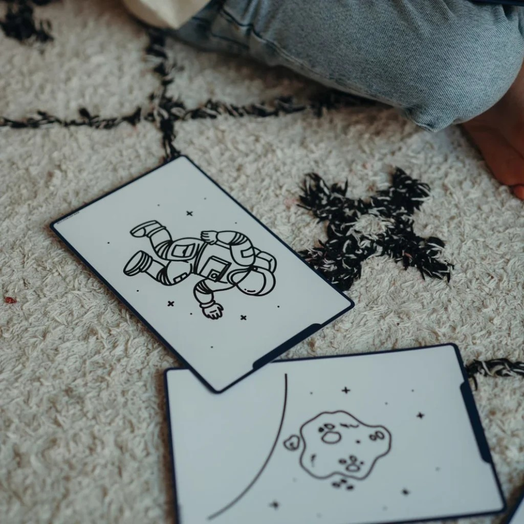 Placas retangulares com desenhos de astronauta e asteroide sobre tapete branco com padrão preto