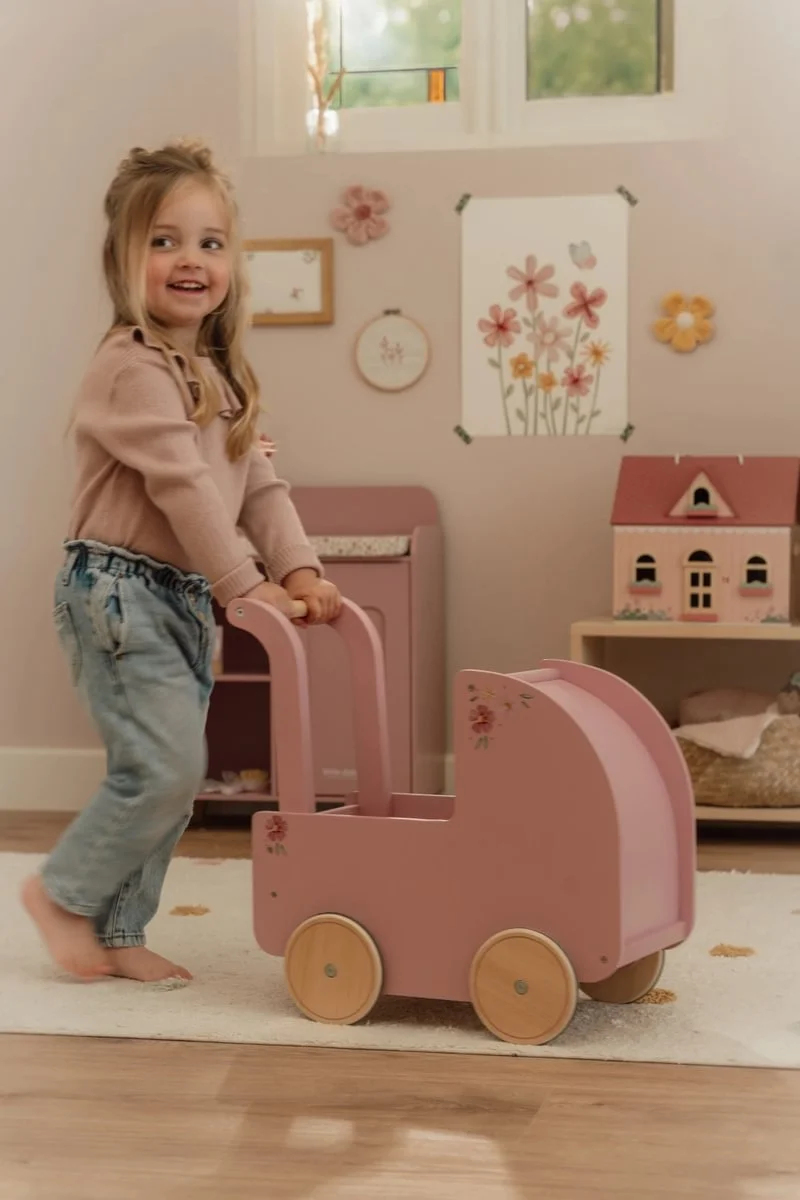Carrinho de madeira cor-de-rosa com detalhes florais segurado por criança num quarto infantil