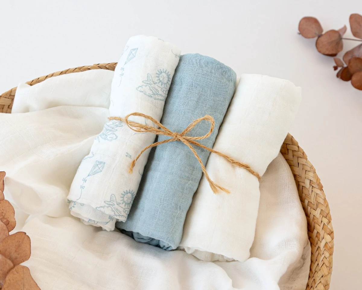 Três panos de tecido fino enrolados e amarrados com corda rústica em cesta de vime