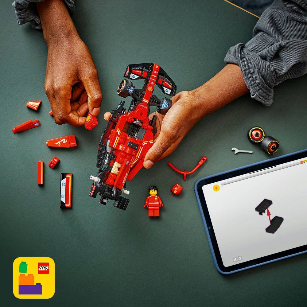 Mãos a montar carro de corrida vermelho LEGO com peças e mini-figura ao lado de tablet com instruções.