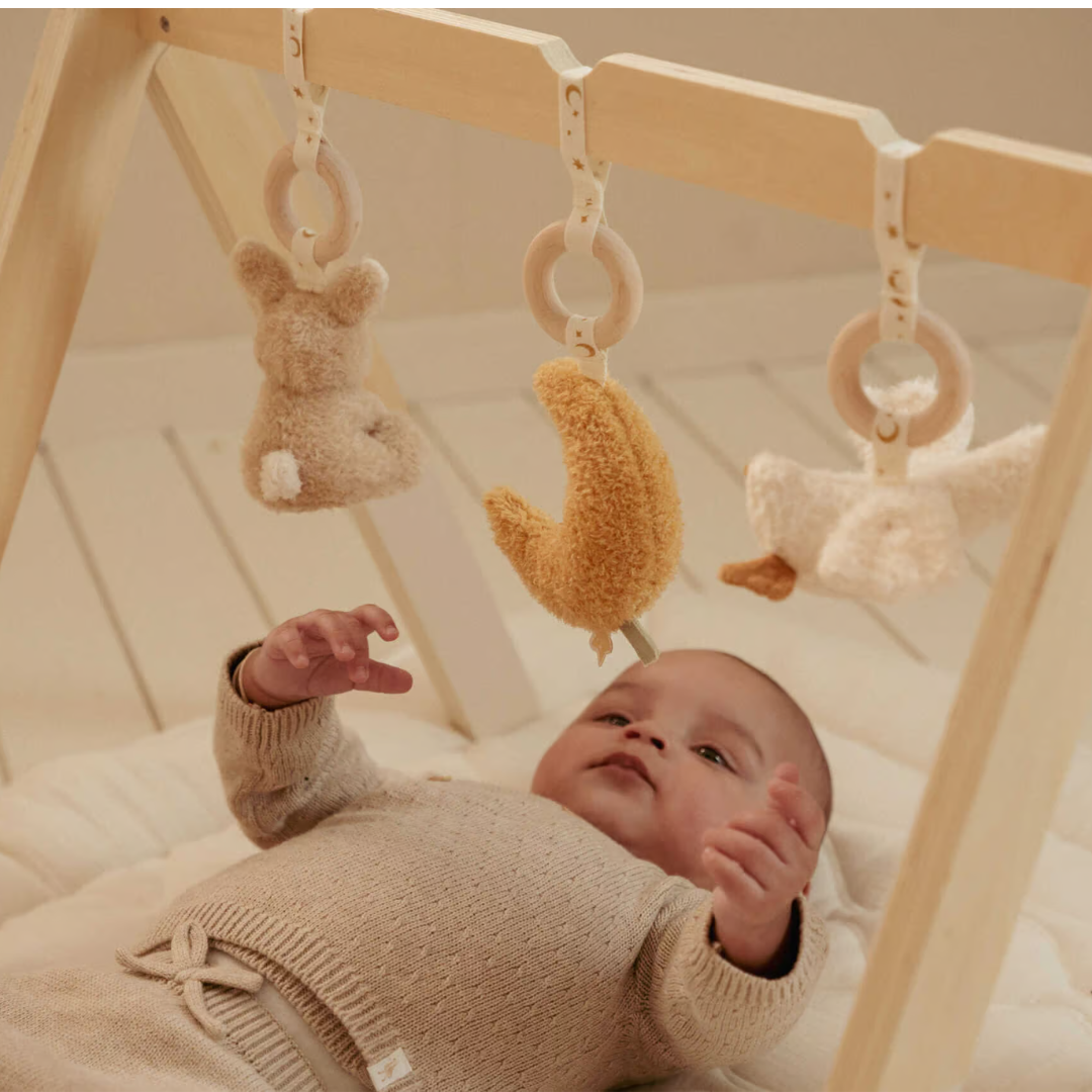 Parque de atividades para bebé em madeira com brinquedos pendurados de pelúcia e bebé deitado a brincar