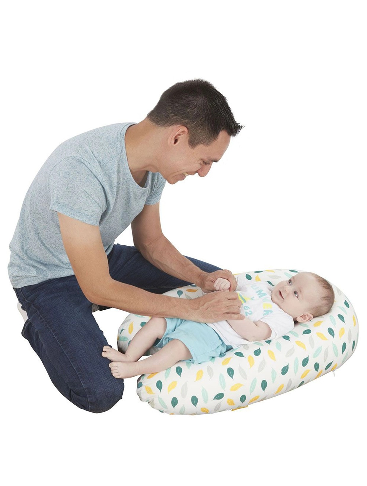 Almofada de apoio para bebé com padrão de folhas coloridas e bebé vestido de branco e azul com adulto a brincar.