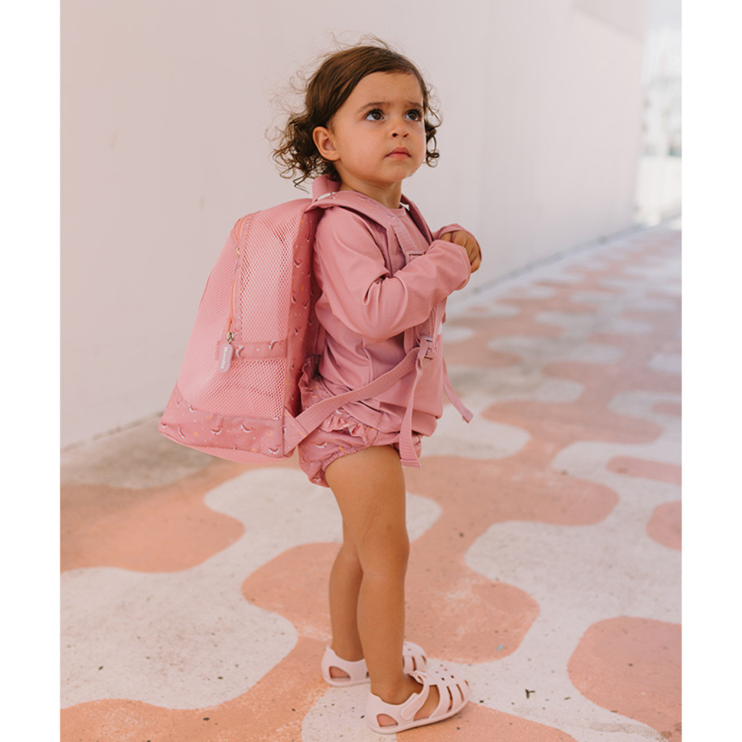 Criança com mochila e roupa cor de rosa em pavimento cor de rosa e branco