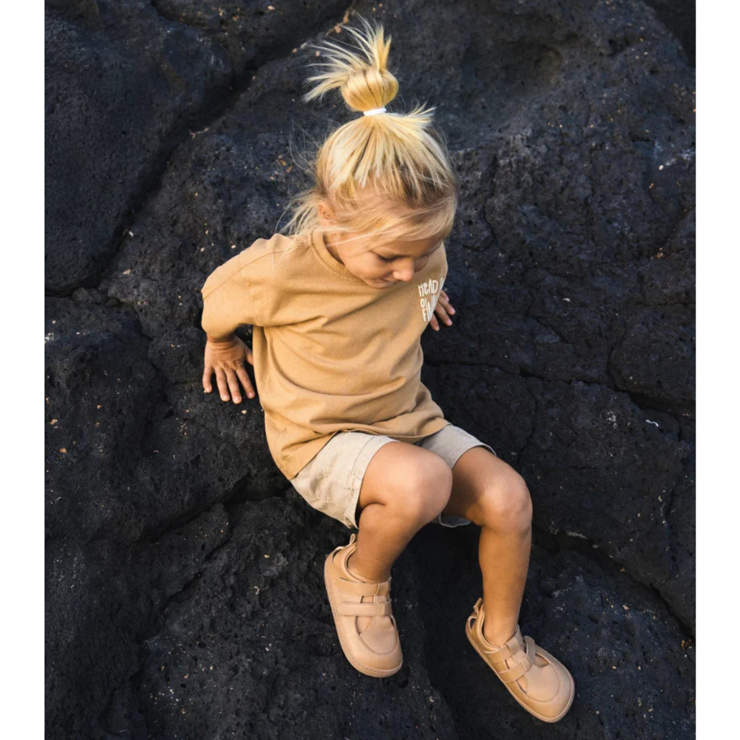 Criança loira vestindo roupa bege sentada em rochas vulcânicas negras