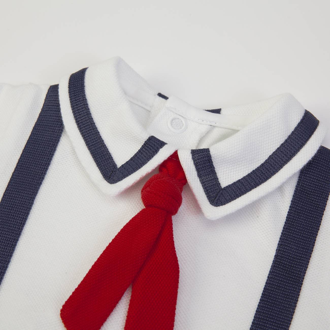 Roupa de bebé branca com gola branca, riscas azuis, gravata vermelha e alças azuis