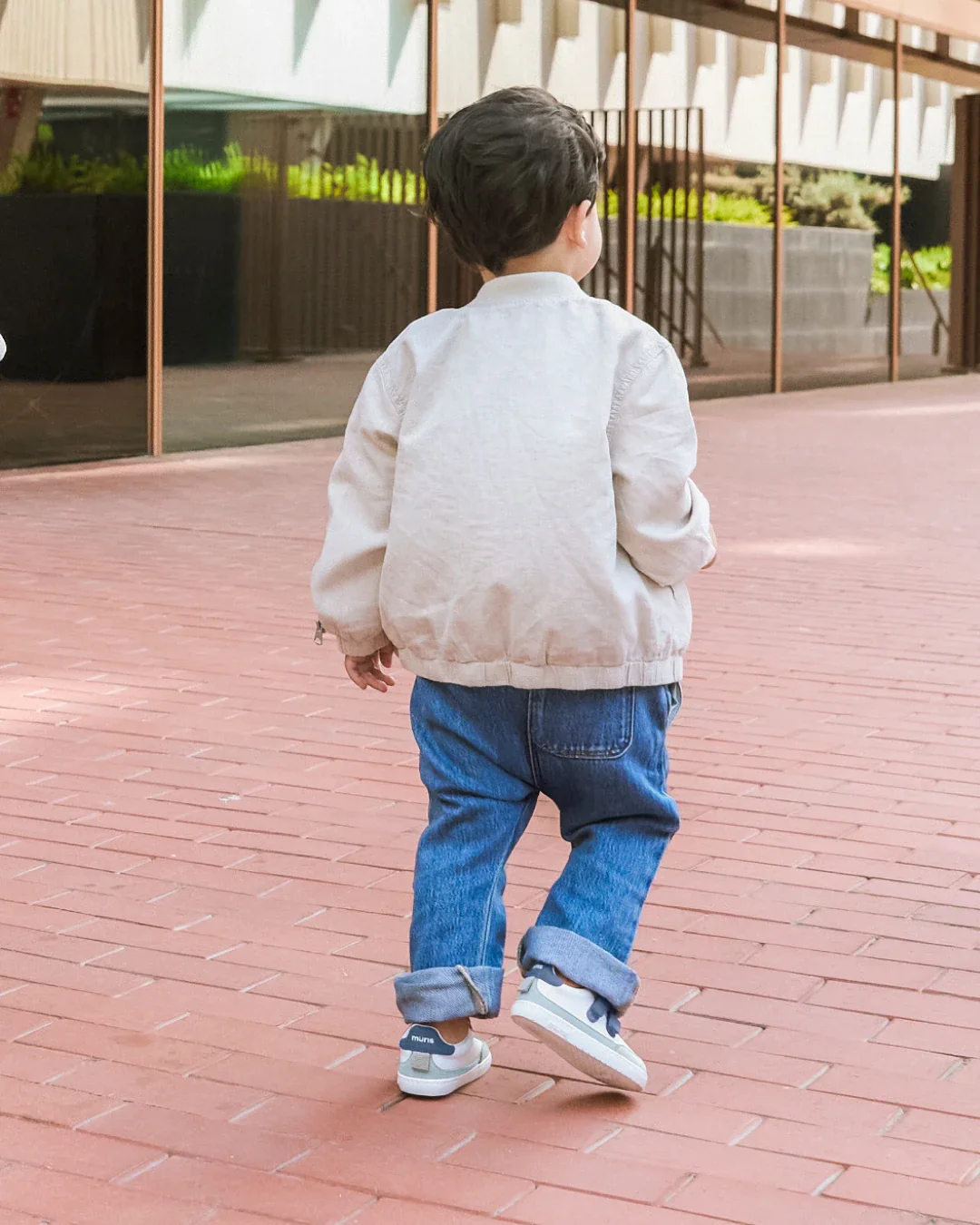 Criança vestindo casaco bege, calças de ganga e sapatilhas com sola de borracha