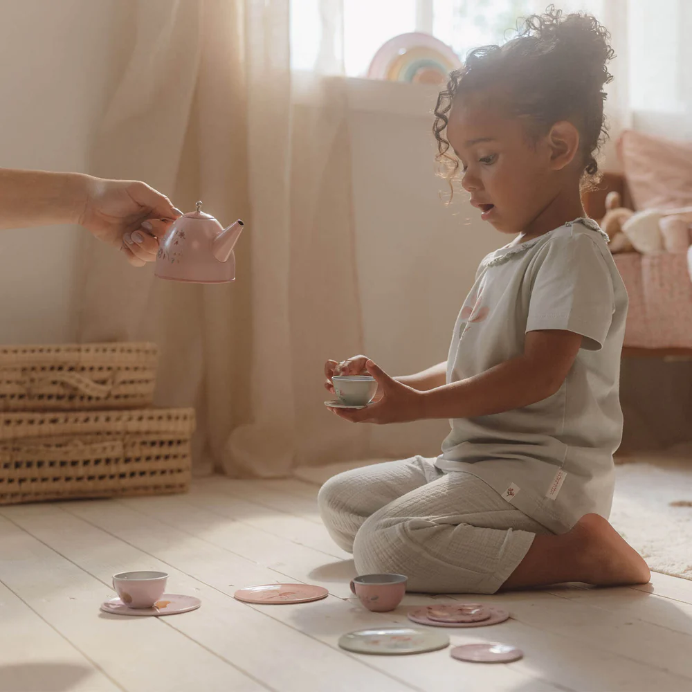 Criança a brincar com jogo de chá infantil de cerâmica cor-de-rosa no chão de madeira clara