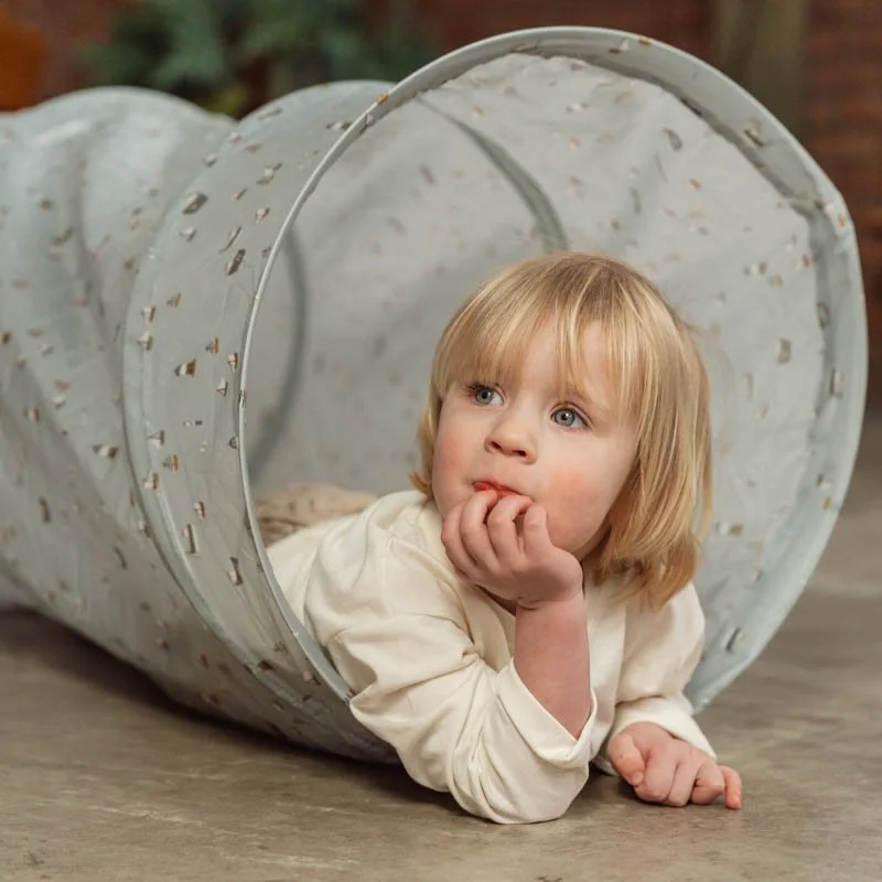 Criança dentro de túnel de brincar de tecido cinza claro com padrões coloridos