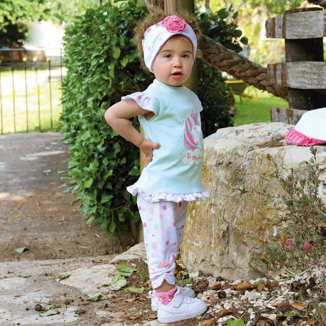 Criança com roupa azul claro e detalhes rosas ao ar livre