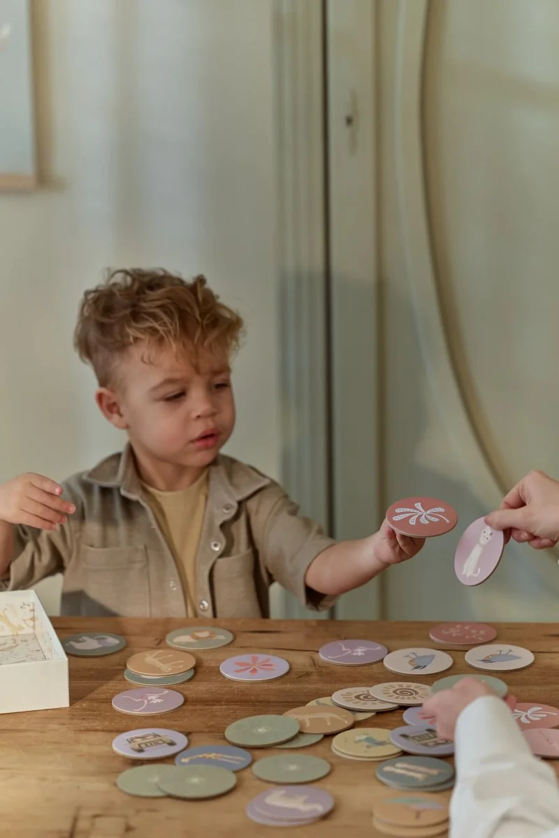 Menino a jogar com cartas redondas coloridas numa mesa de madeira