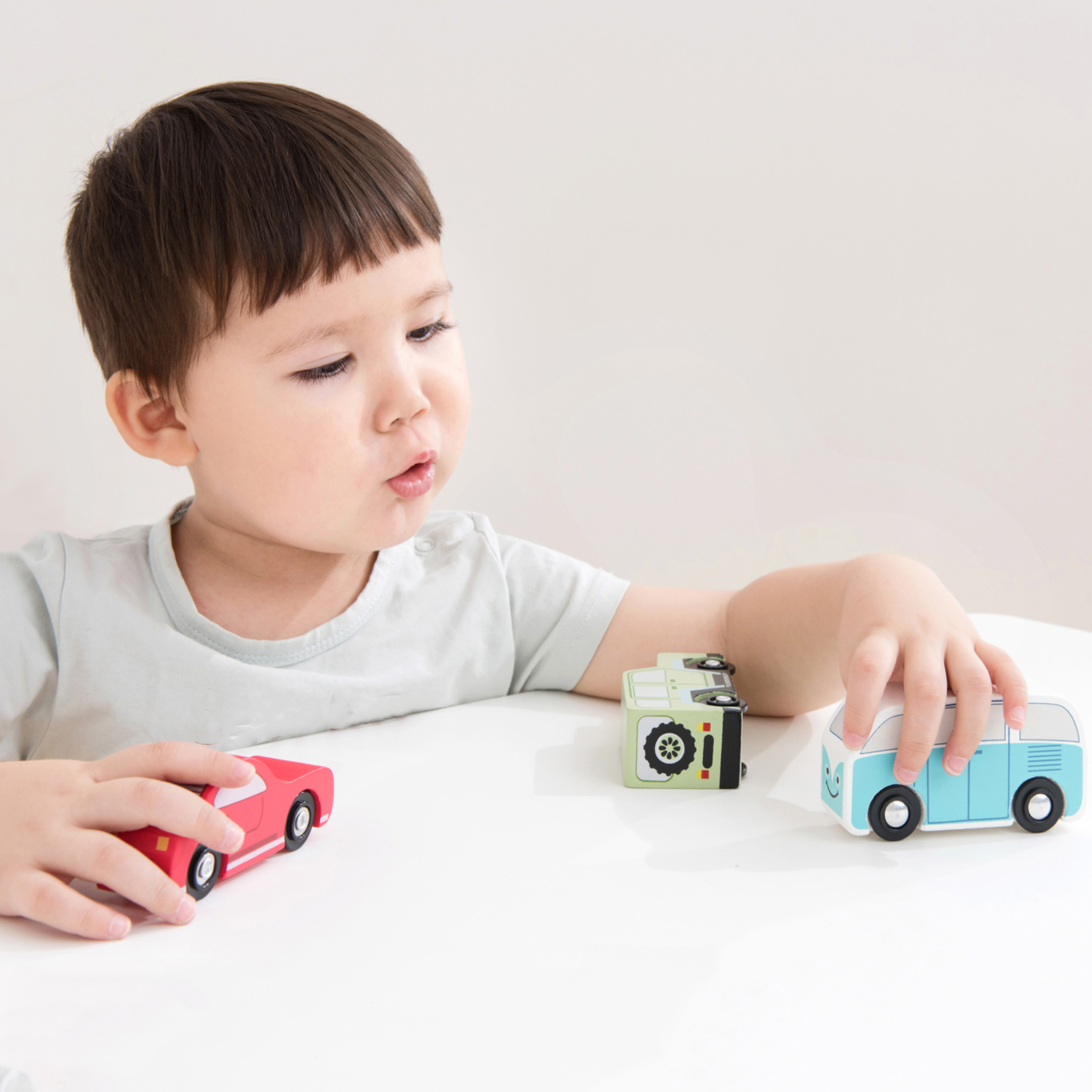 Criança a brincar com carros de brinquedo de madeira coloridos sobre mesa branca