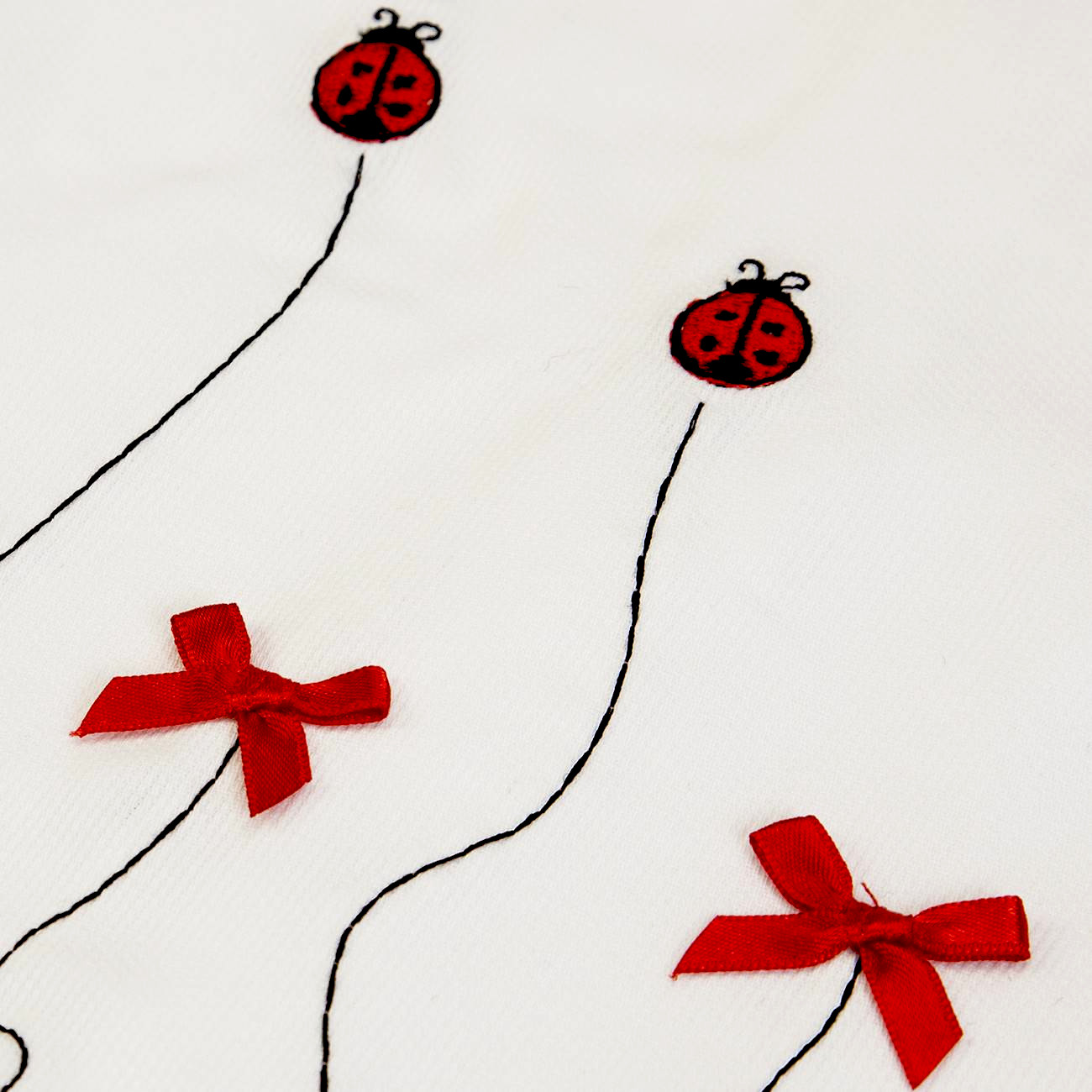 Tecido branco com bordados de joaninhas e laços vermelhos