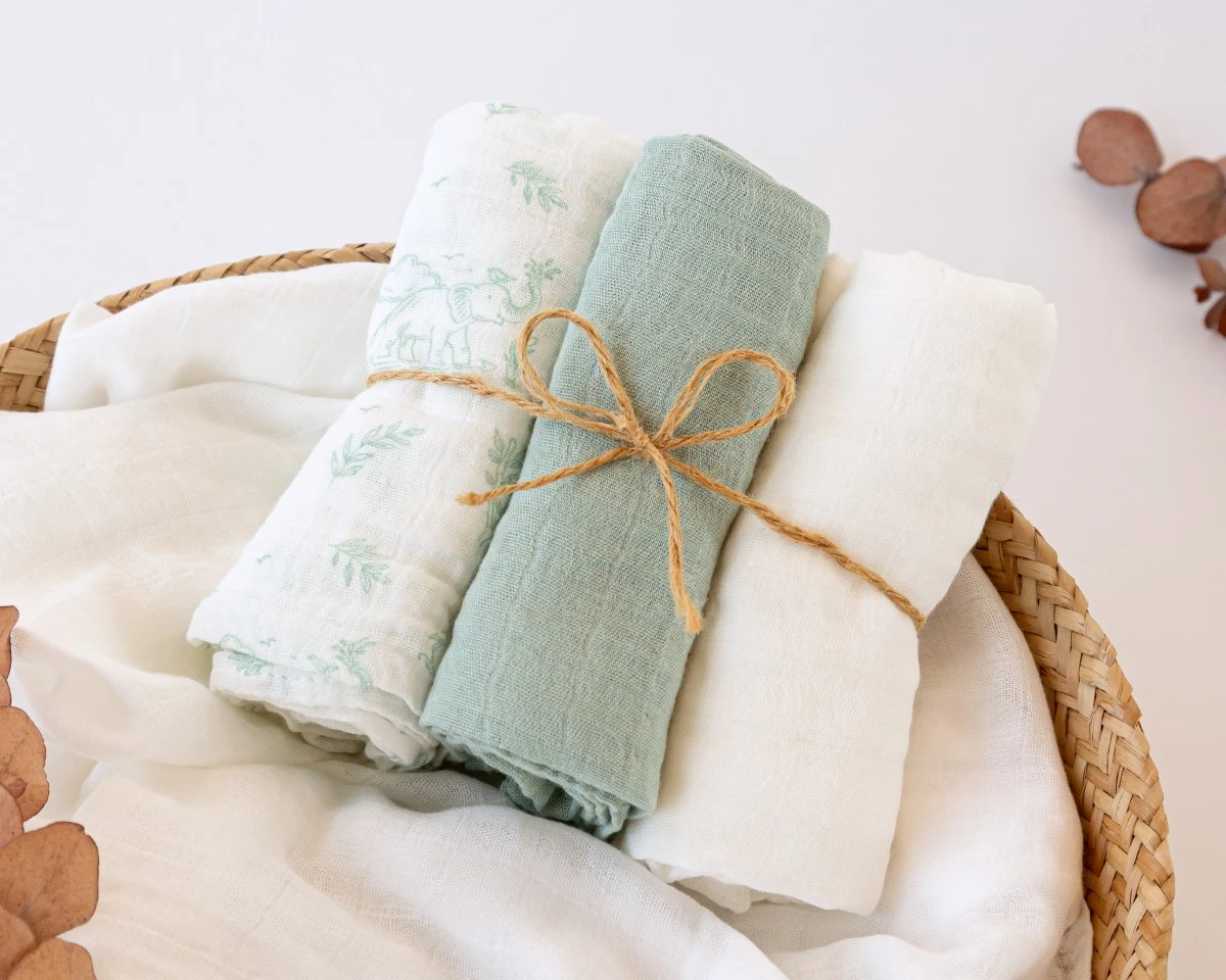 Conjunto de três panos enrolados em branco e verde com corda dentro de cesto de vime