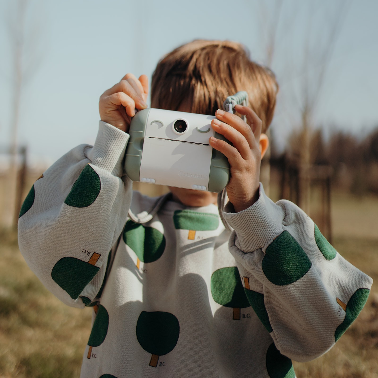 Criança com câmara fotográfica instantânea e sweatshirt com padrão de árvores verdes