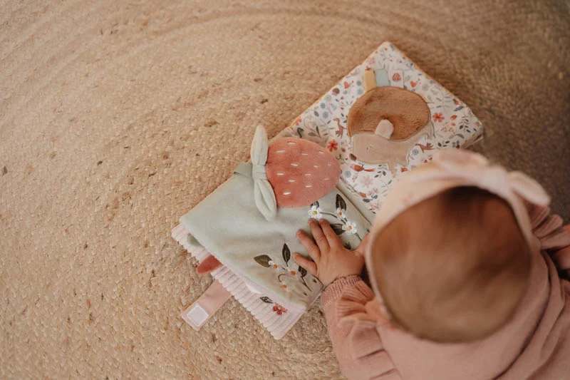Brinquedo sensorial para bebé em tecidos macios coloridos, com bebé a tocar num tapete redondo de fibra natural