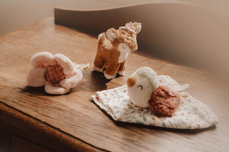 Três brinquedos de peluche: flor, veado e pássaro sobre mesa de madeira.