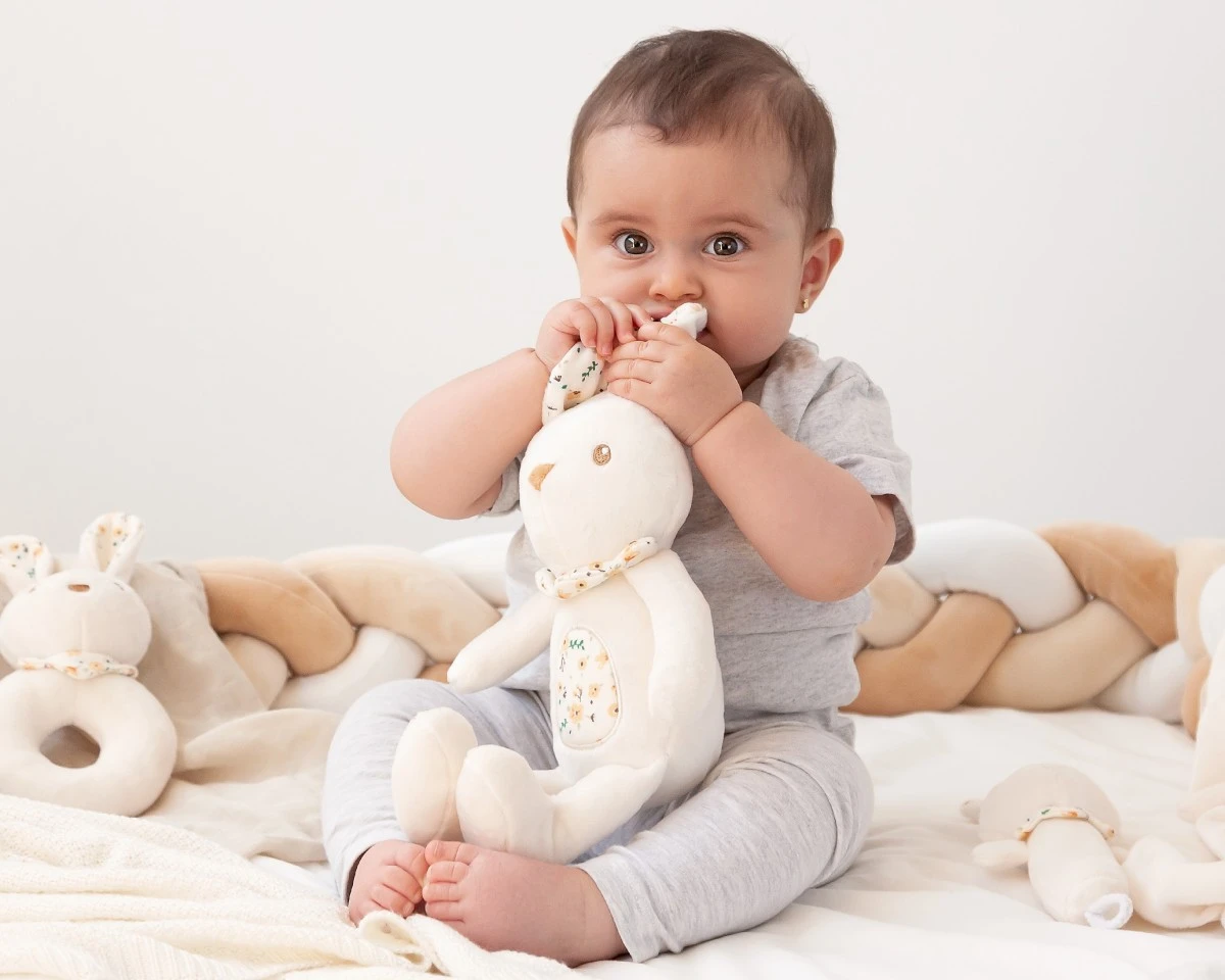 Bebé com brinquedo de peluche coelho branco sentado em berço acolchoado creme e bege