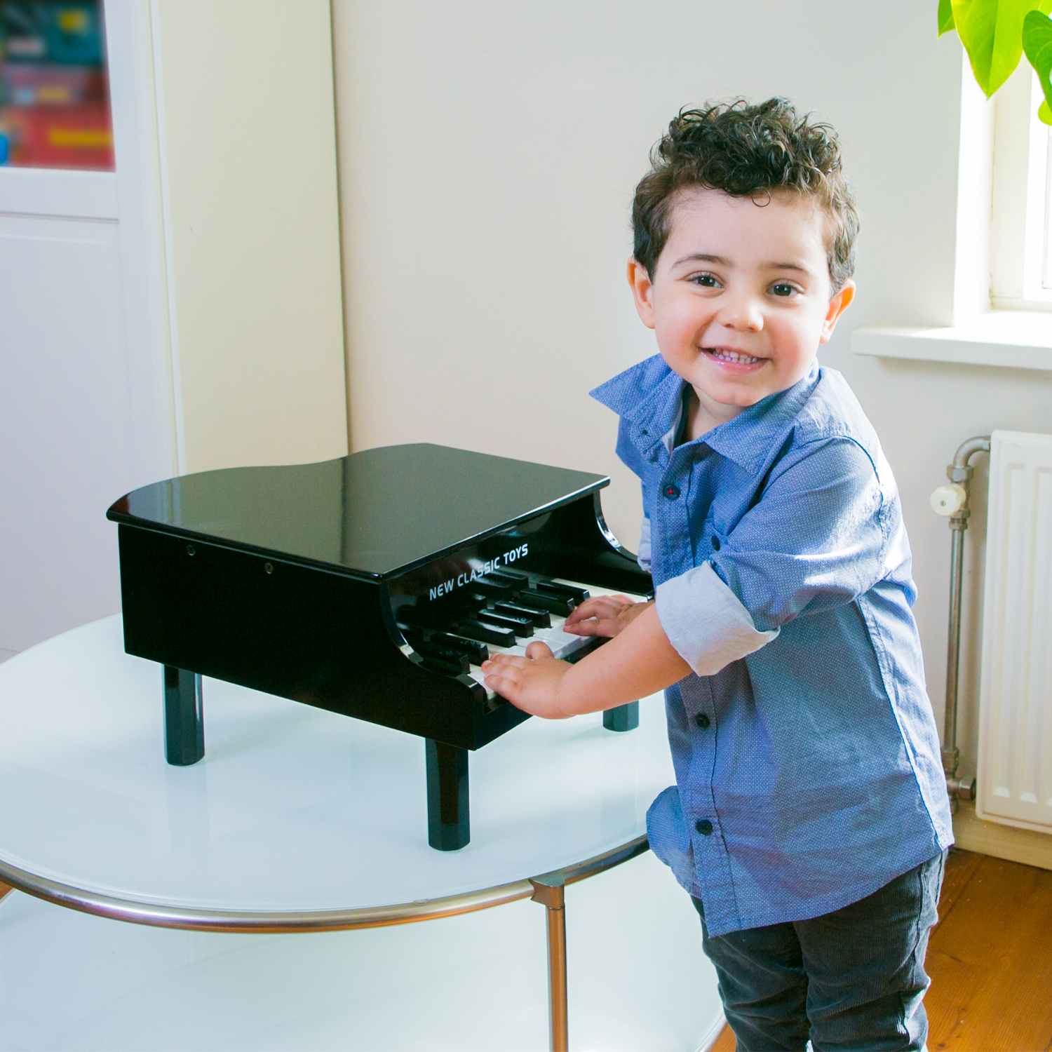 Menino ao lado de piano de brinquedo preto sobre mesa branca