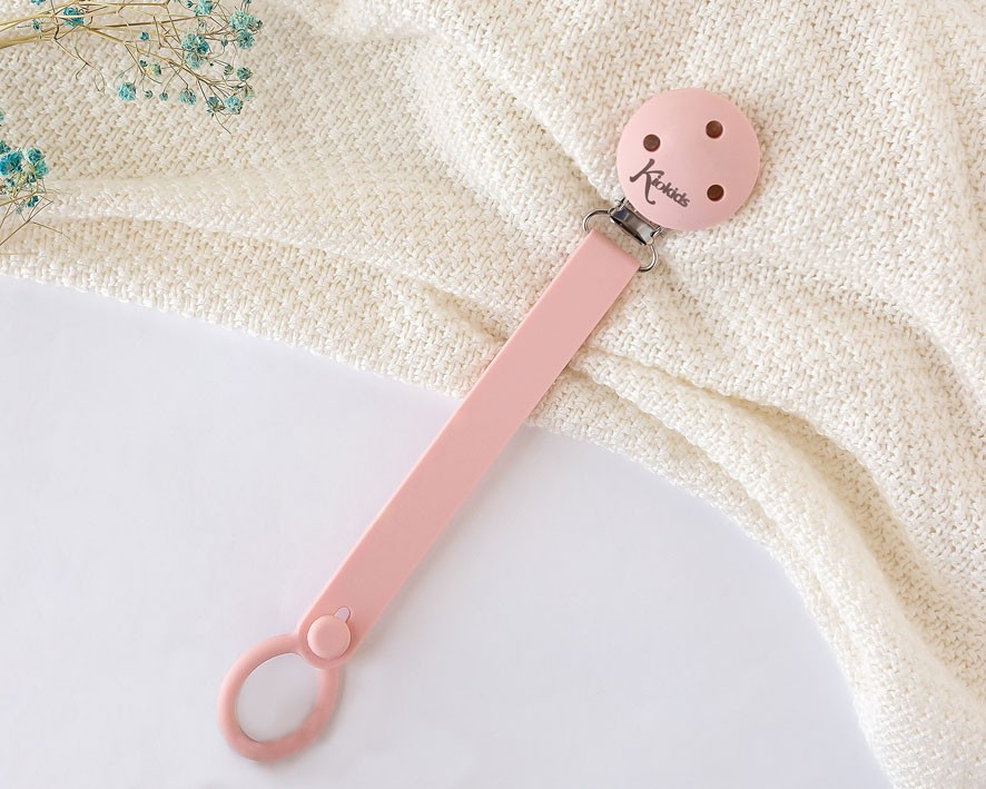 Prendedor de chupeta rosa com fecho metálico sobre tecido branco texturizado