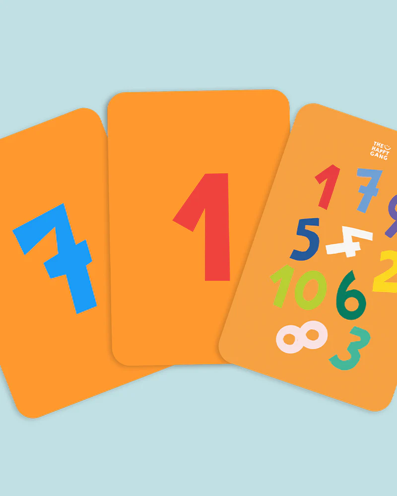 Três cartas de jogo com números coloridos em fundo laranja sobre superfície azul clara.