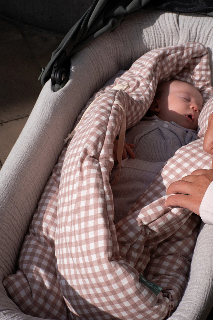 Berço acolchoado cinza com bebé em saco de dormir xadrez rosa e branco
