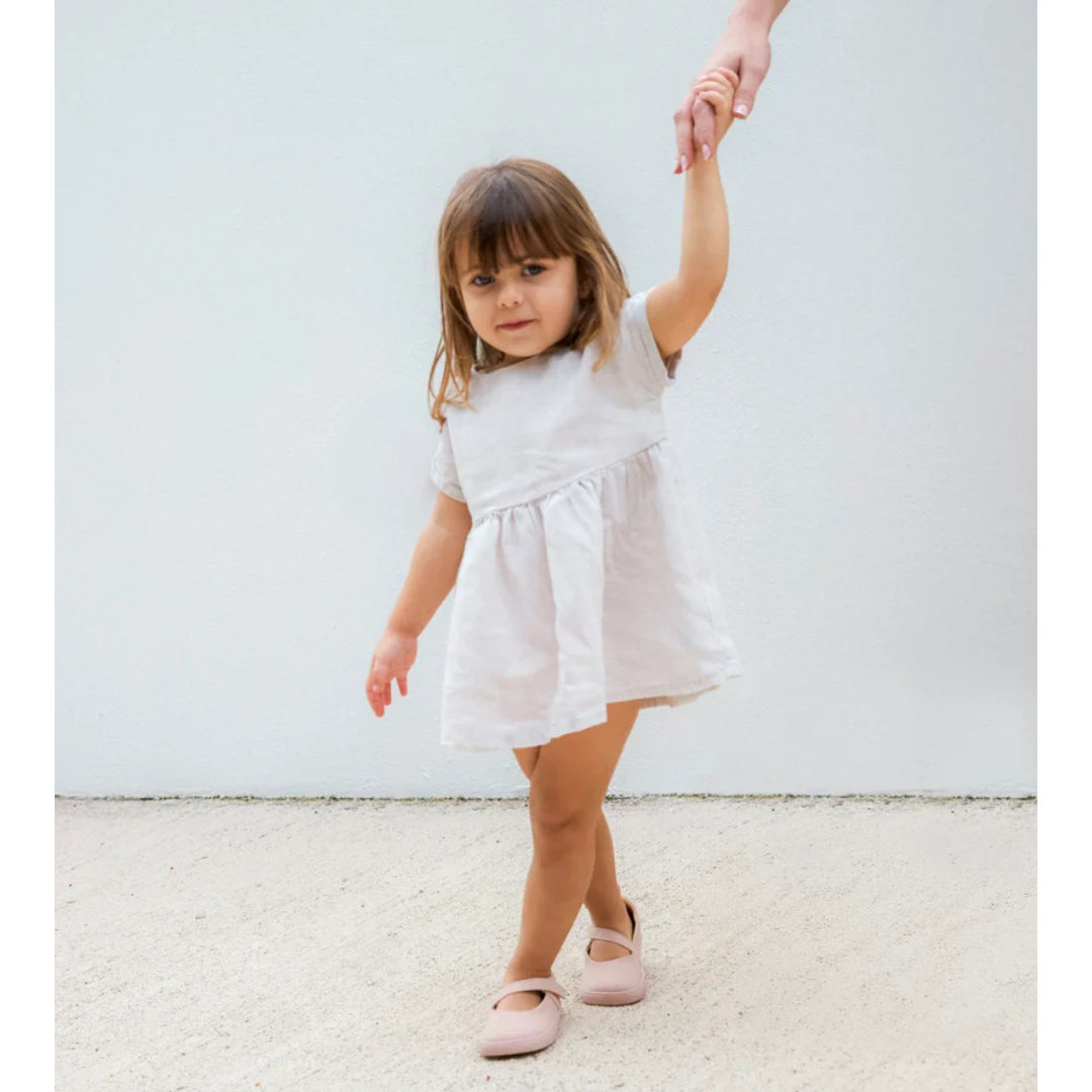 Criança com vestido branco e sapatos rosa segurando a mão de um adulto