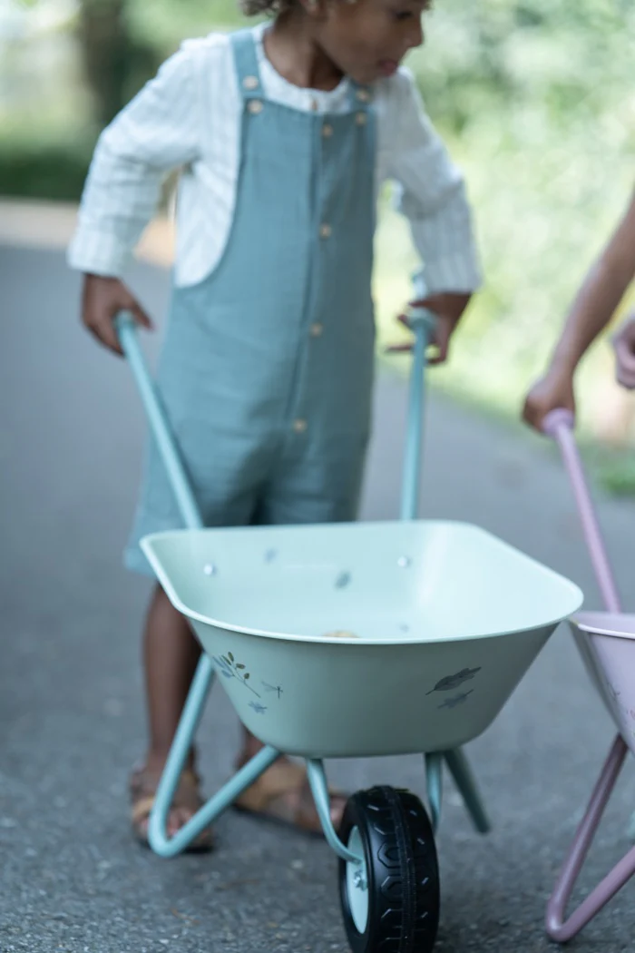 Carrinho de mão infantil azul claro com pintura floral sendo empurrado por criança na rua