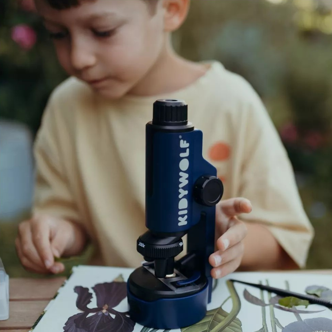 Microscópio azul KIDYWOLF na mesa com ilustrações botânicas em uso por criança