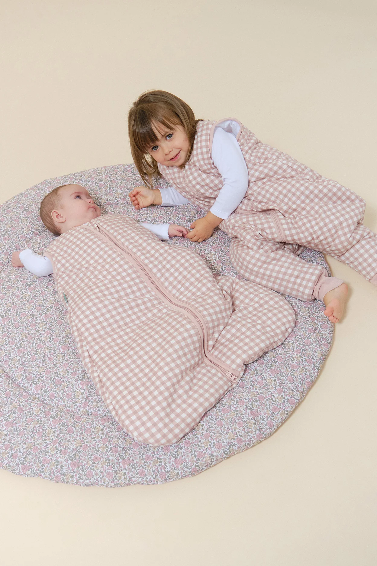 Bebés com roupas de dormir xadrez rosa e branco numa almofada floral redonda