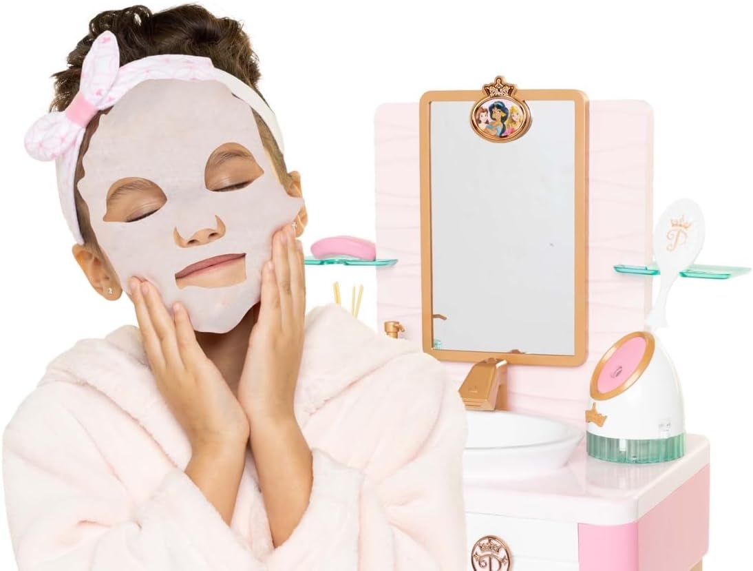 Criança com máscara facial branca e roupão rosa na frente de lavatório de brinquedo rosa e branco com espelho