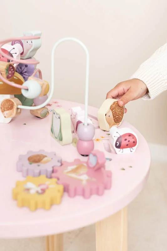 Mesa rosa com brinquedos de madeira infantil e mão a segurar peça