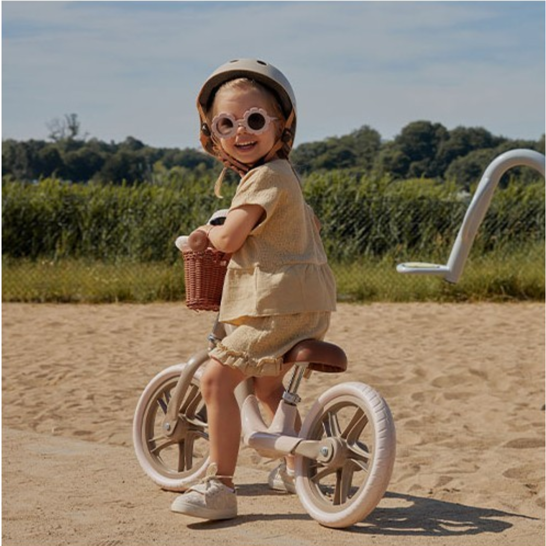 Criança de capacete e óculos em bicicleta branca num caminho de areia